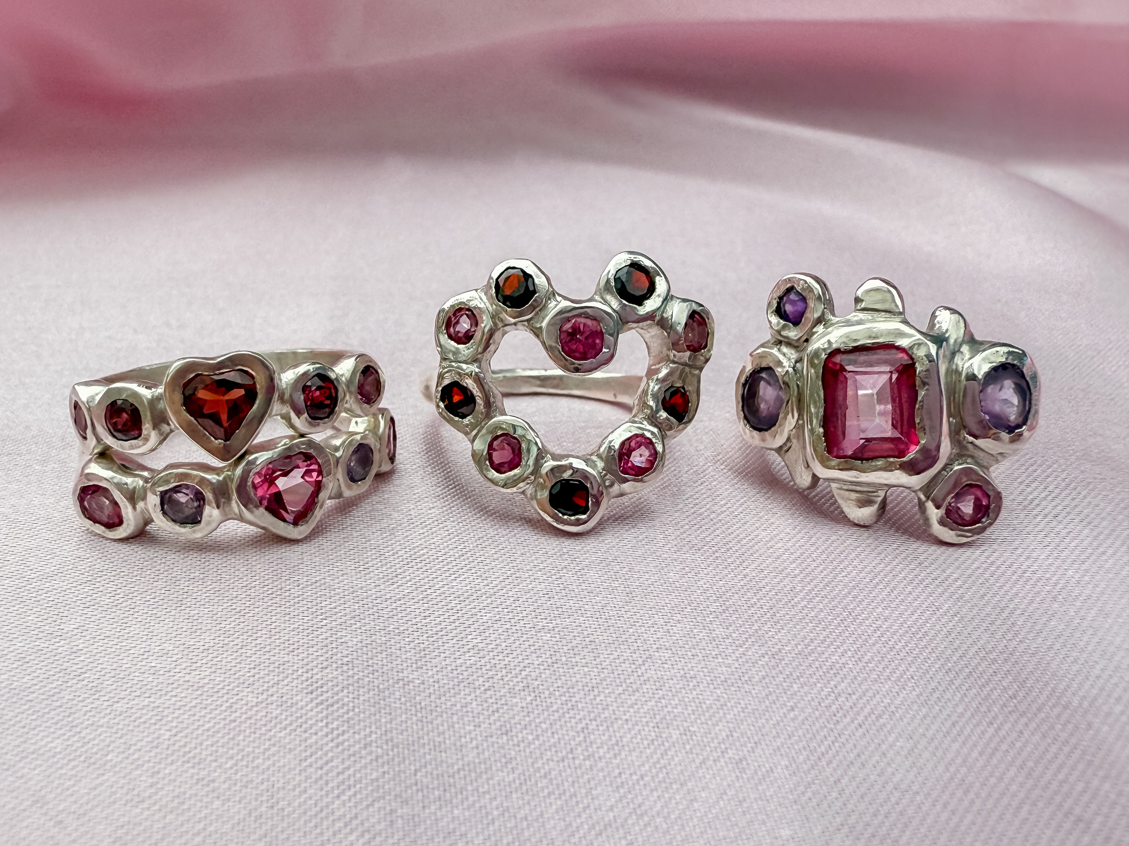 Silver rings made with pink, red and purple gemstones on a pink silk background