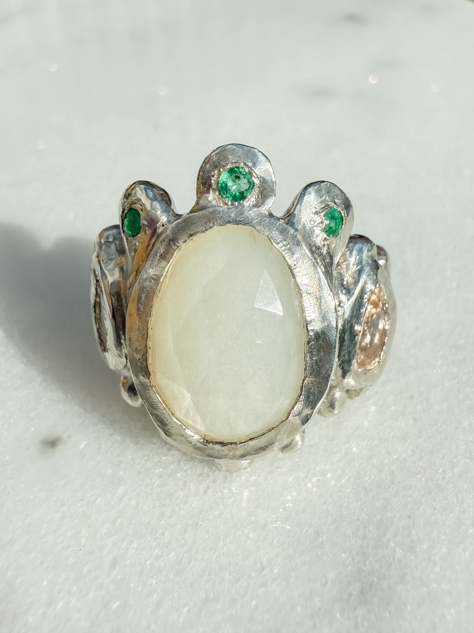 Silver ring with a large central stone and smaller stones on a light background
