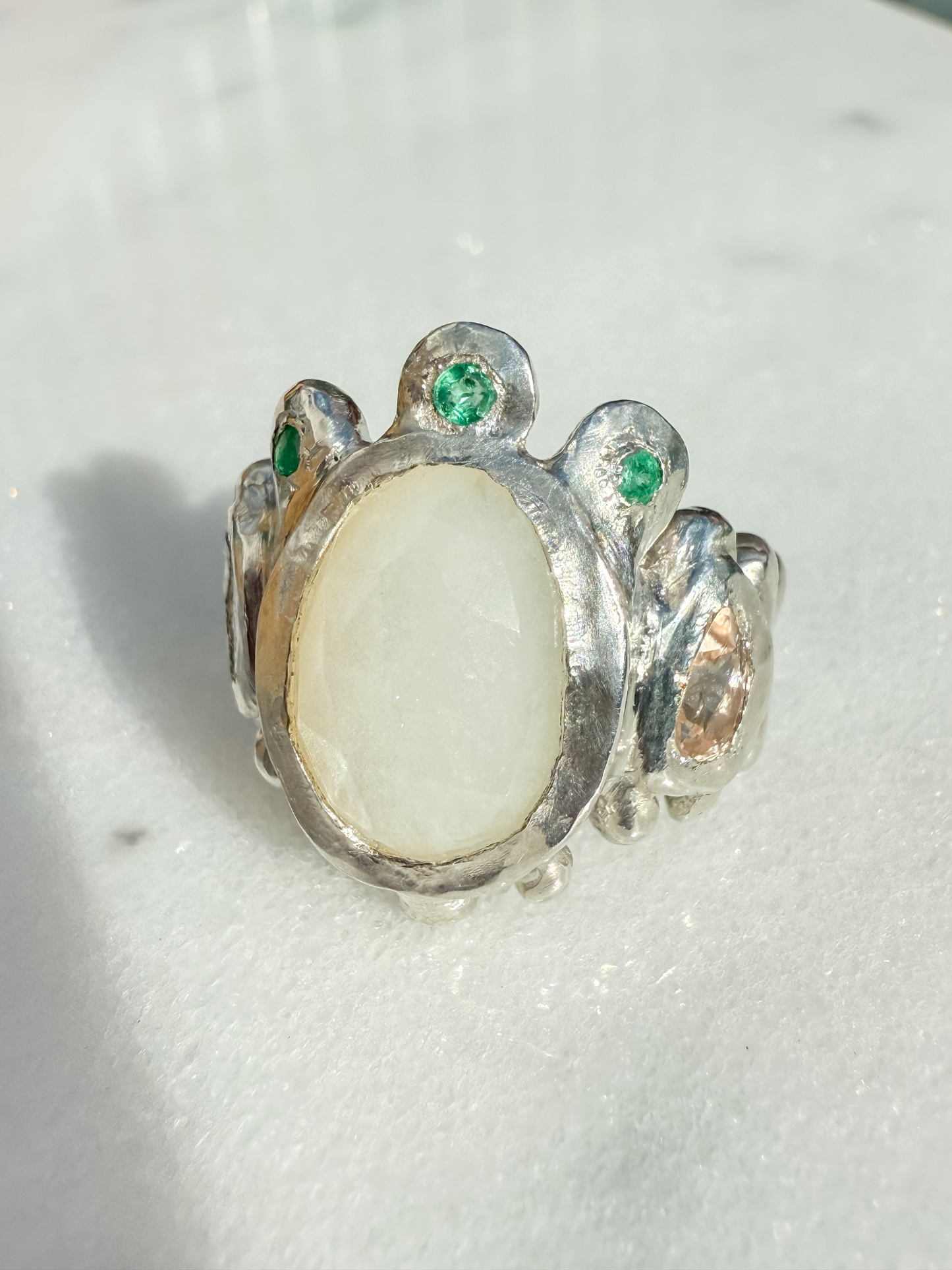 Silver ring with a large central stone and smaller stones on a white background