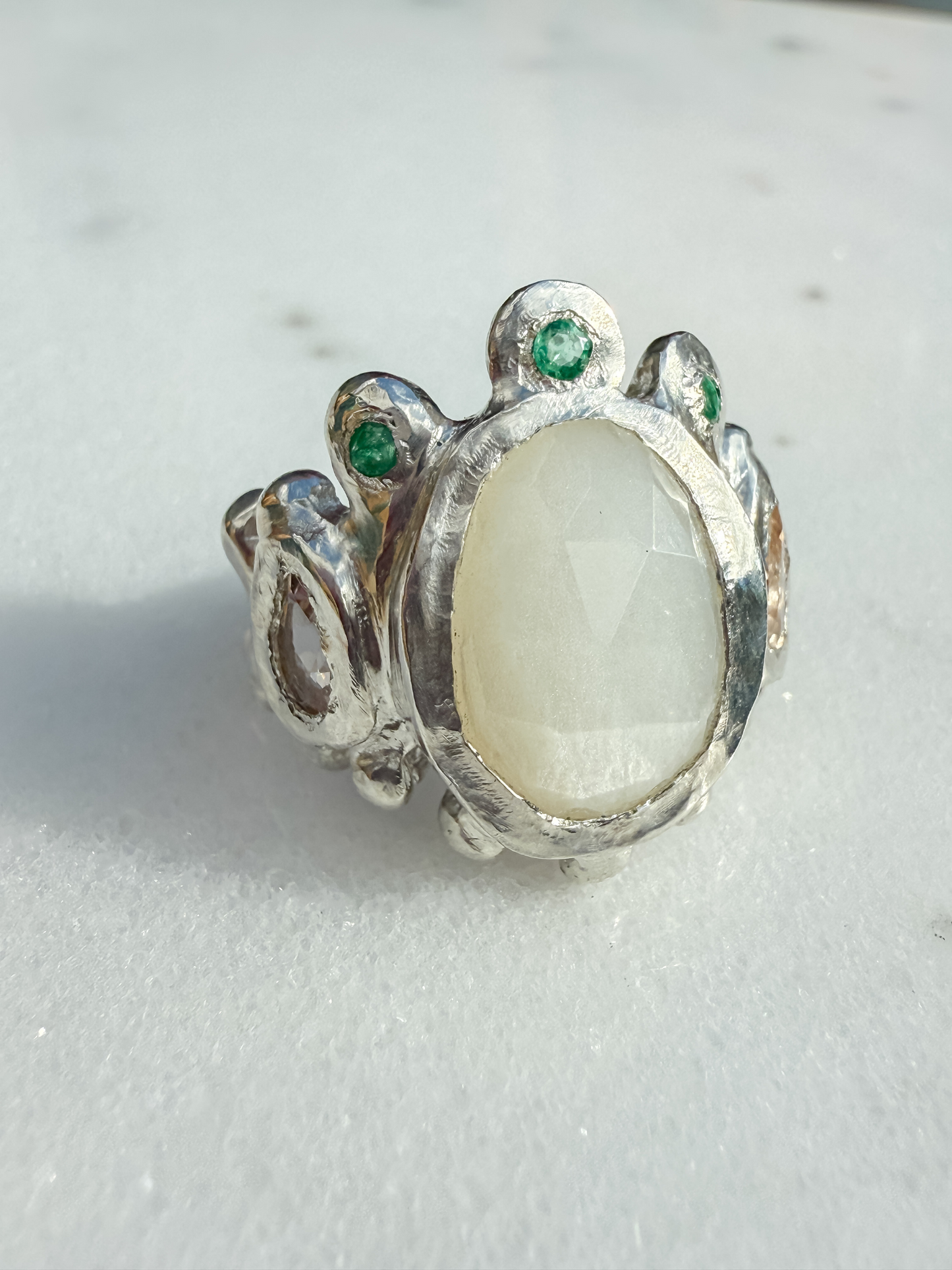 Silver ring with a large central stone and smaller stones on a light gray background