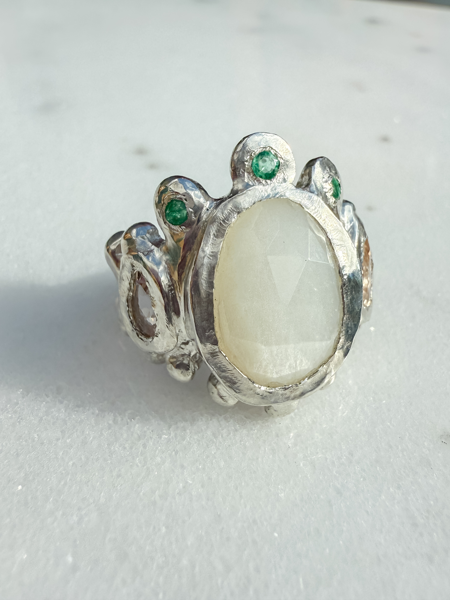 Silver ring with a large central stone and smaller stones on a light gray background