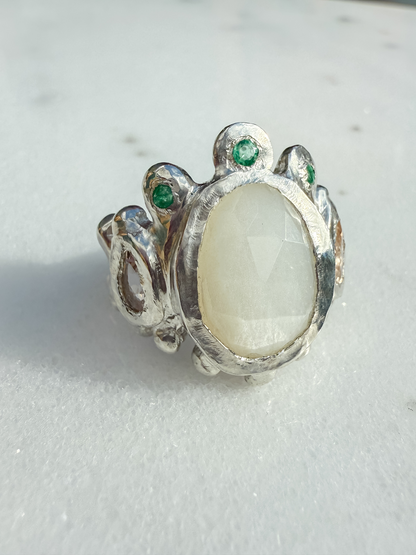 Silver ring with a large central stone and smaller stones on a light gray background