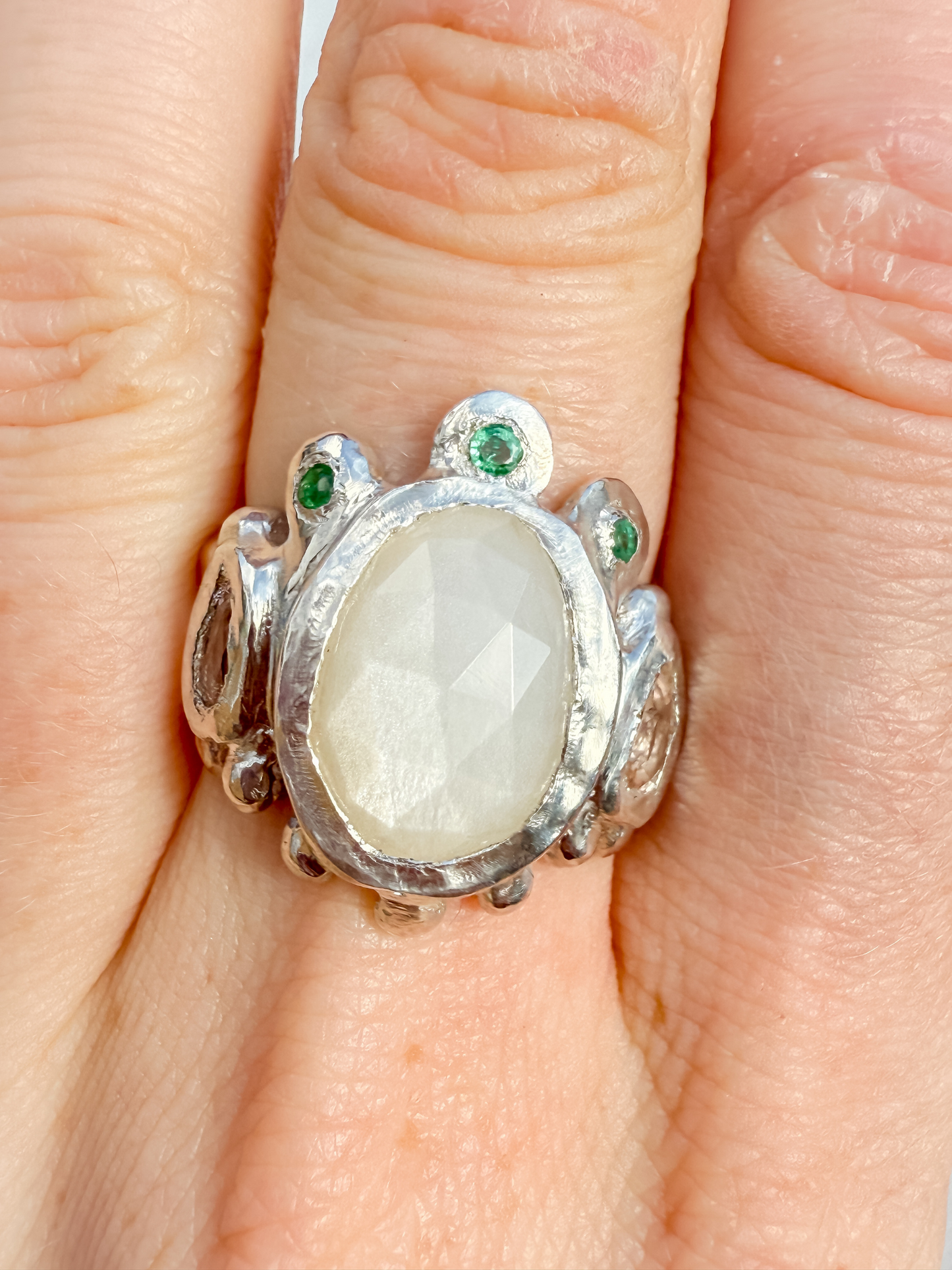 Silver ring with a large central stone and smaller stones on a finger