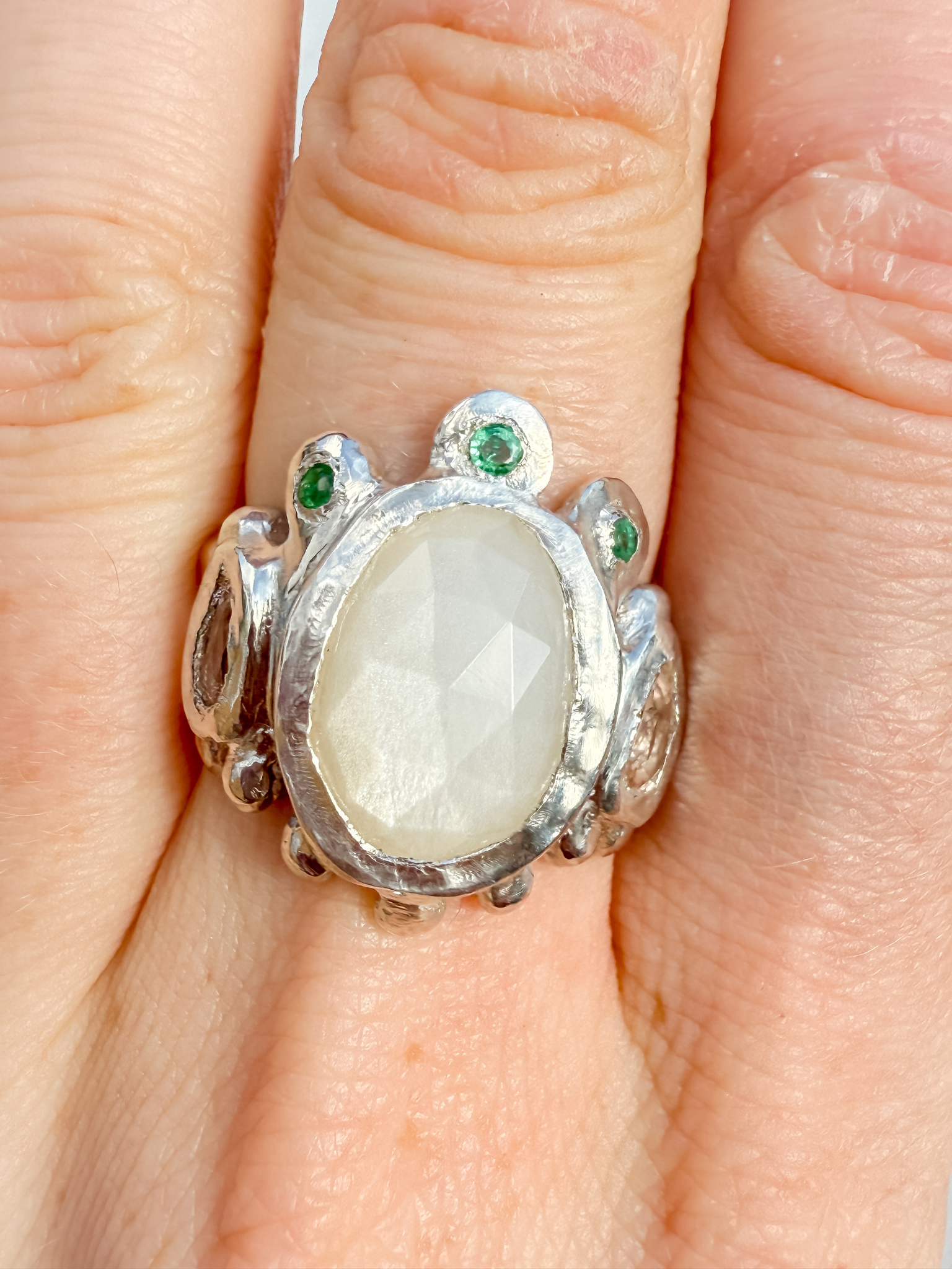 Silver ring with a large central stone and smaller stones on a finger