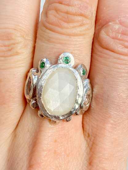 Silver ring with a large central stone and smaller stones on a finger