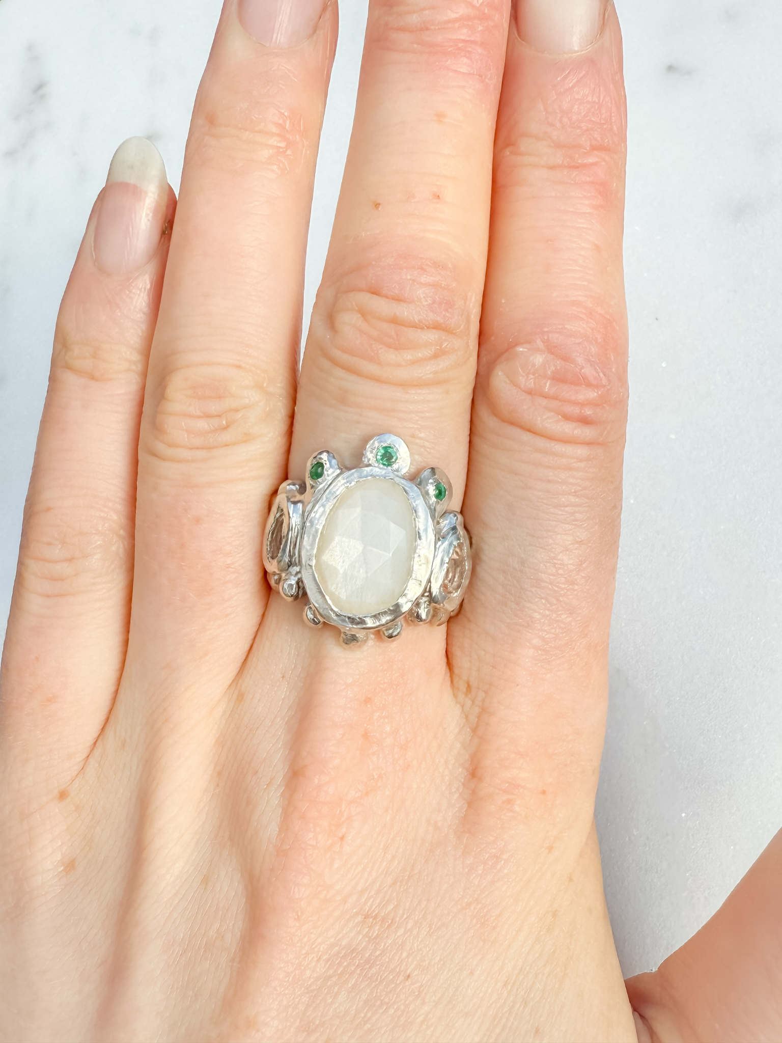 Silver ring with a large central stone and smaller stones on a hand against a light background