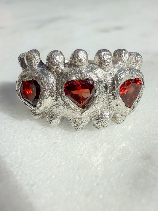 Silver ring with three red heart gemstones on a white background