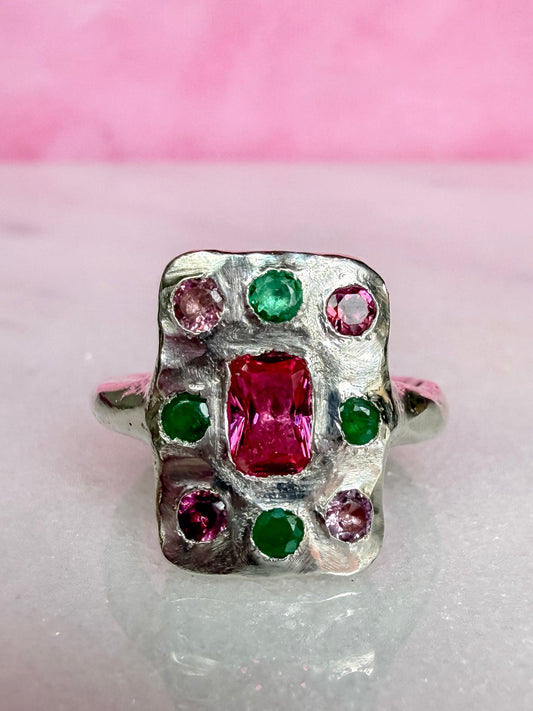 Silver ring with red and green gemstones on a pink and white background