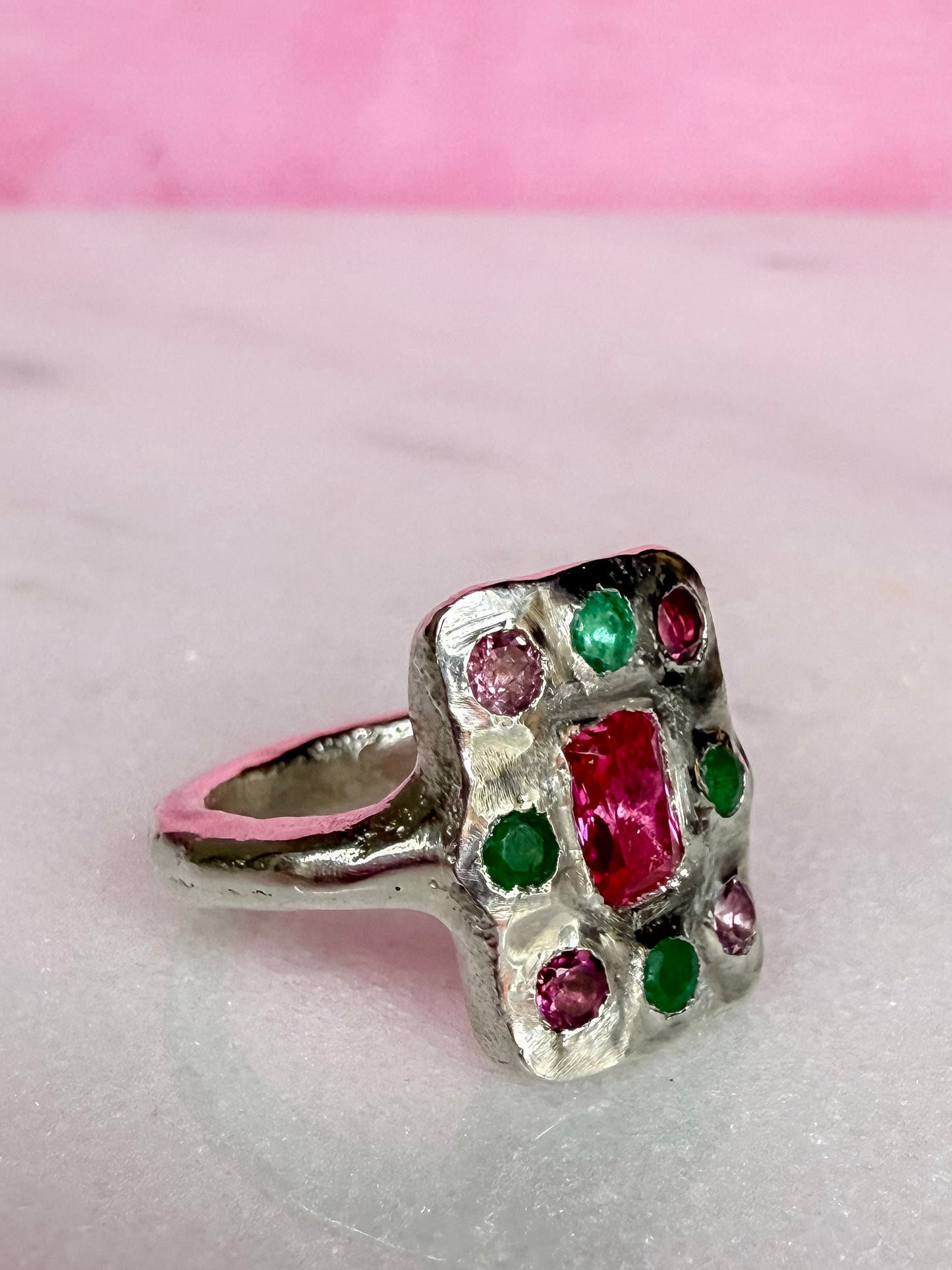 Oblong handmade Silver ring with red, green and pink gemstones on a pink background