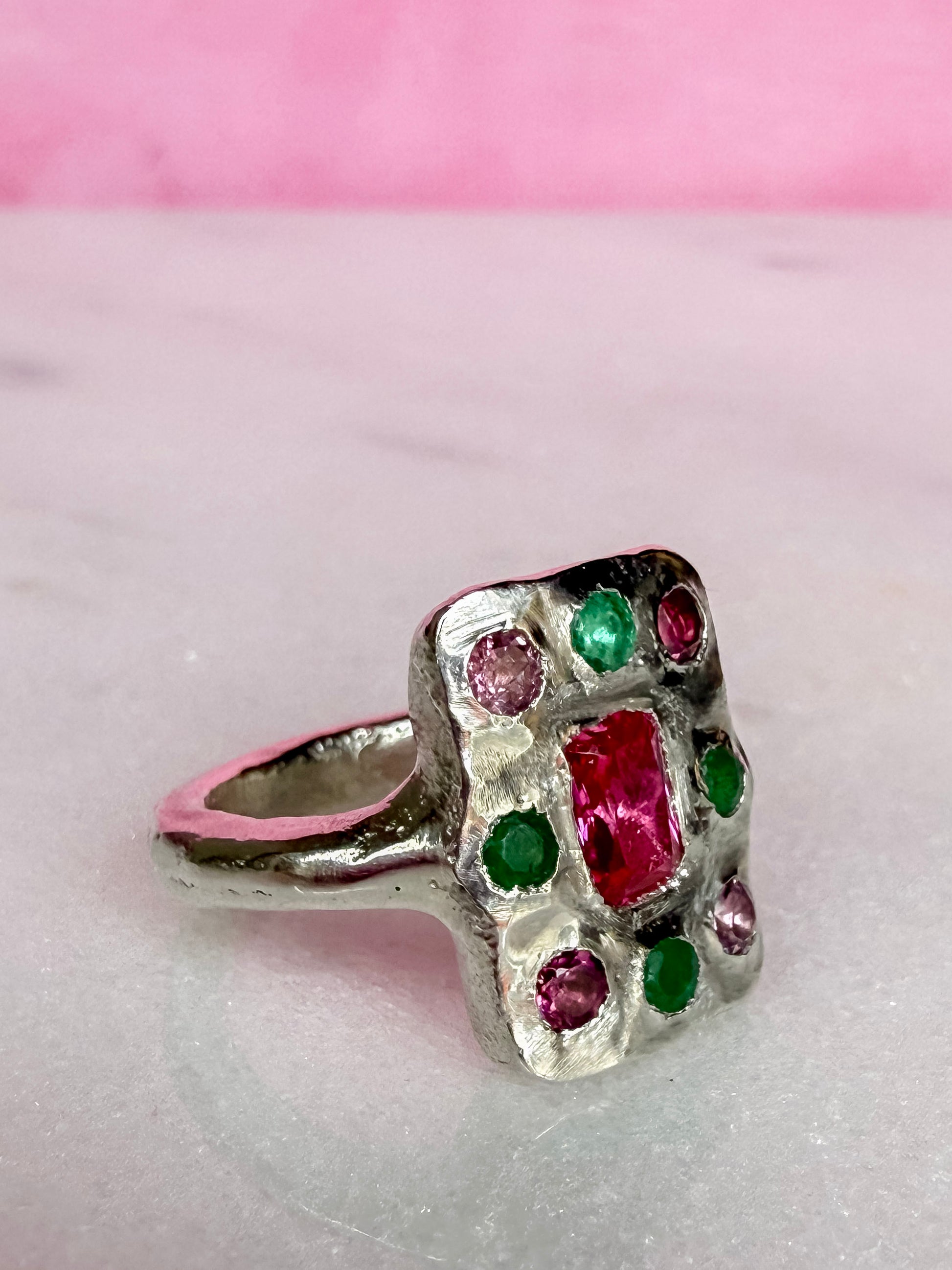 Oblong handmade Silver ring with red, green and pink gemstones on a pink background