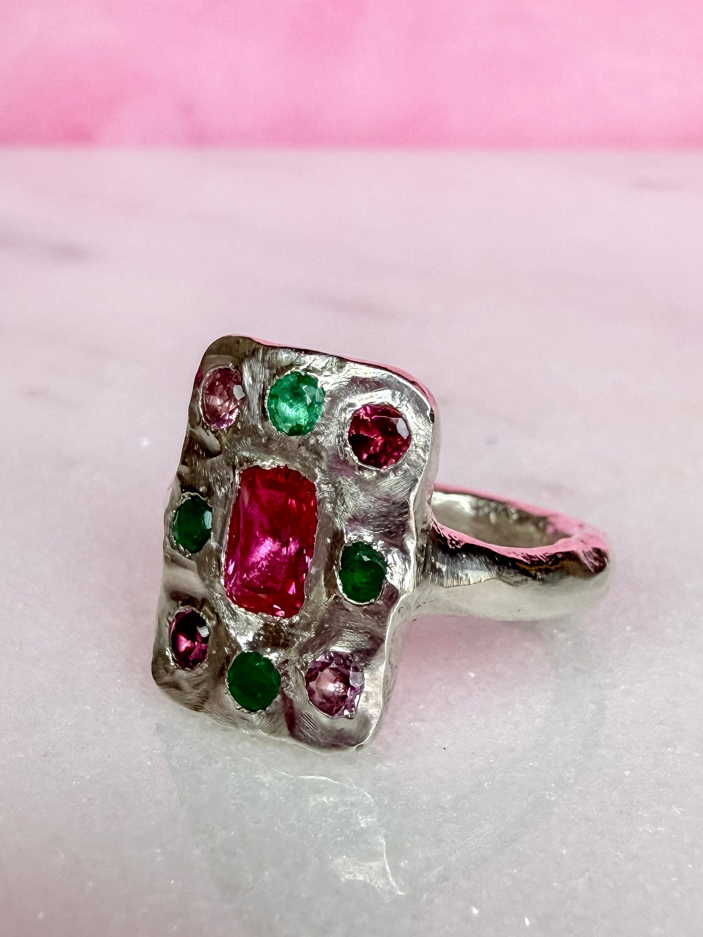 Oblong silver handmade ring with ruby, emerald and pink tourmaline gemstones on marble surface