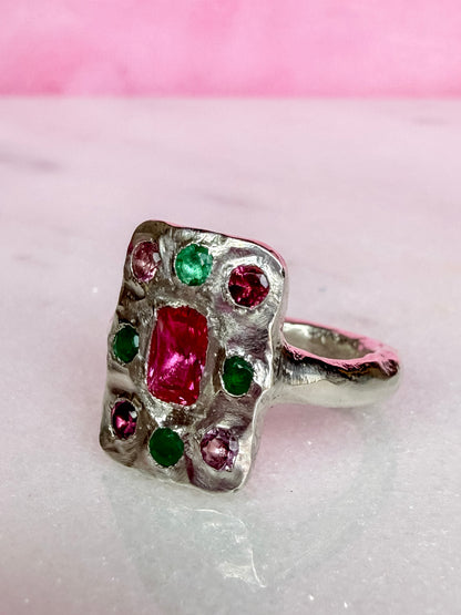Oblong silver handmade ring with ruby, emerald and pink tourmaline gemstones on marble surface