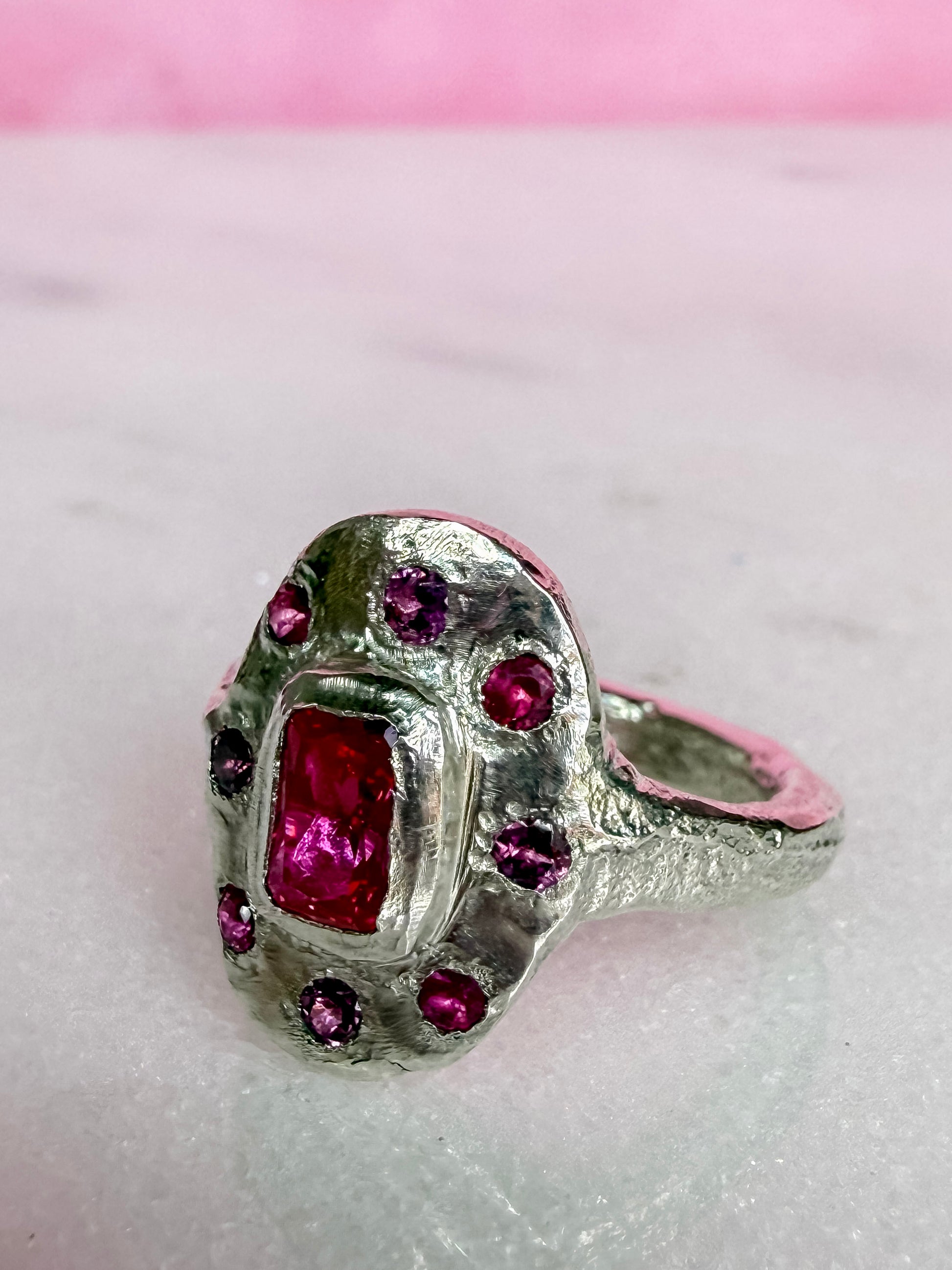 Lab ruby, rhodolite and ruby handmade silver oval ring on marble surface side view 2