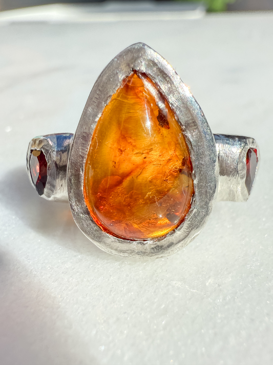 Teardrop-shaped amber stone set in a silver ring on a white background