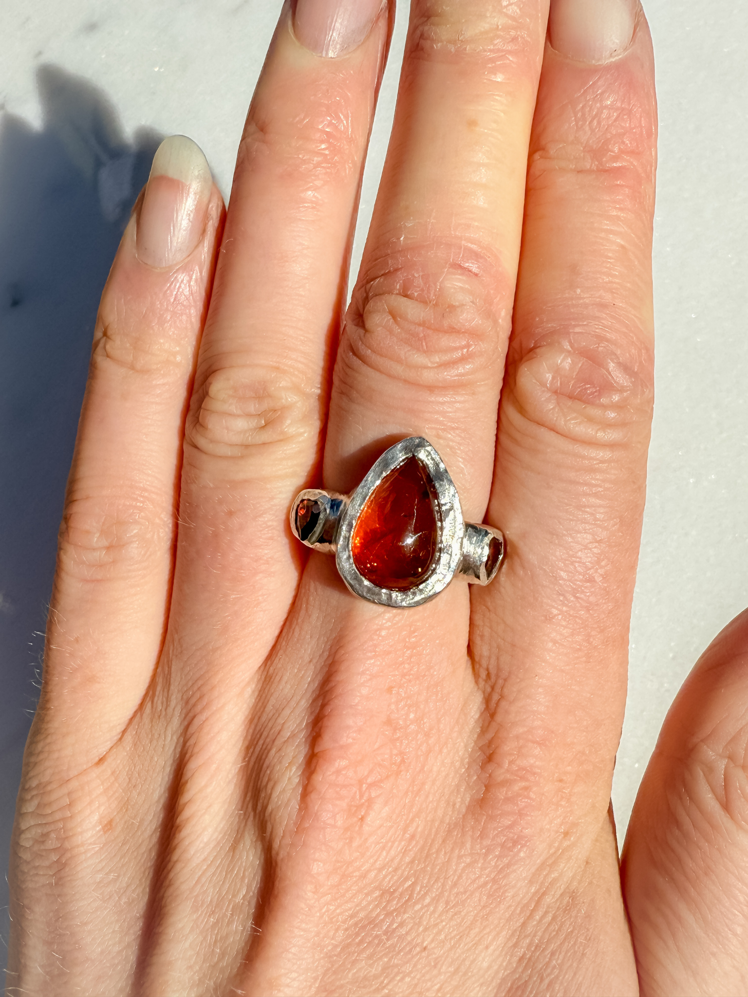 Hand wearing a silver ring with an amber stone on a light background
