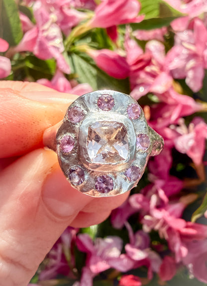 Ring with pink gemstones held in front of pink flowers