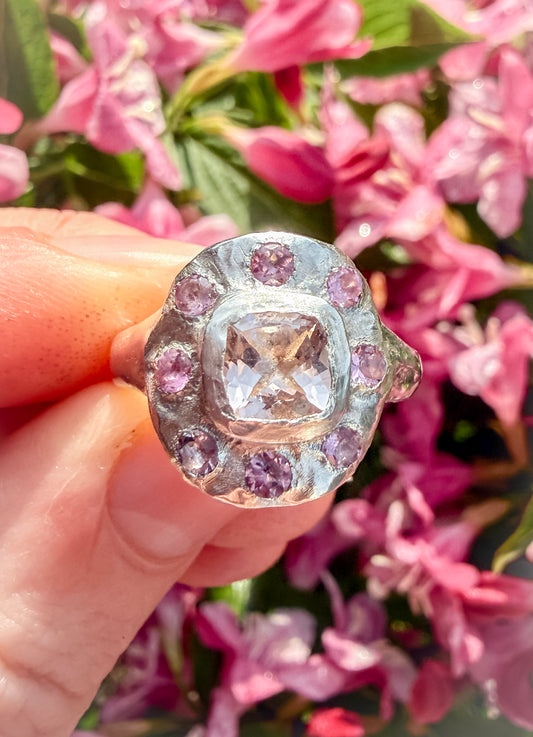 Ring with pink gemstones held in front of pink flowers