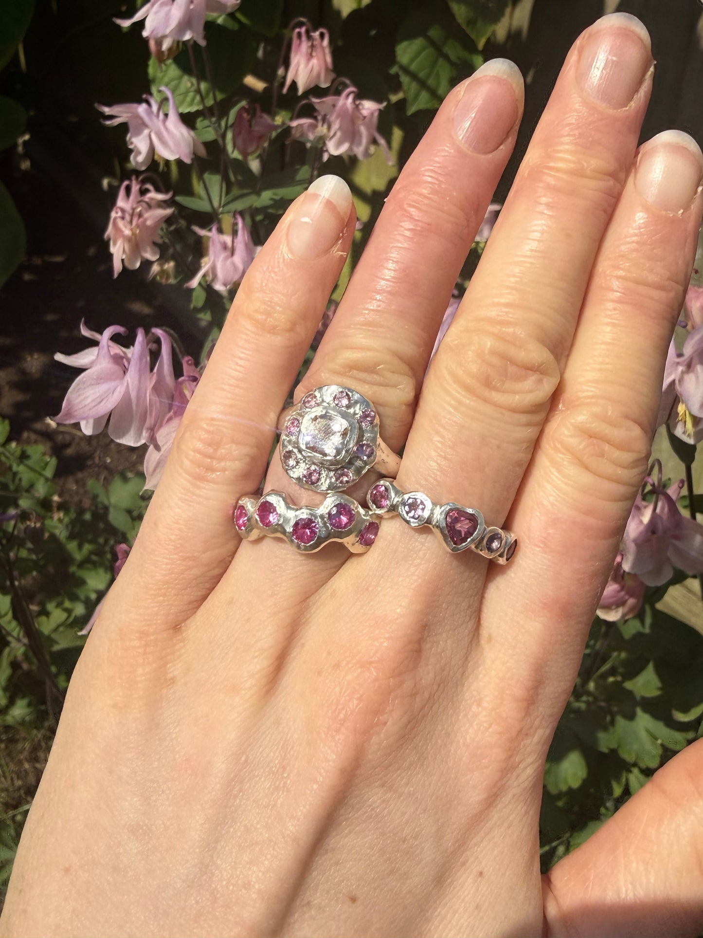 Hand wearing a silver ring with a large peach morganite and smaller gemstones against a floral background.