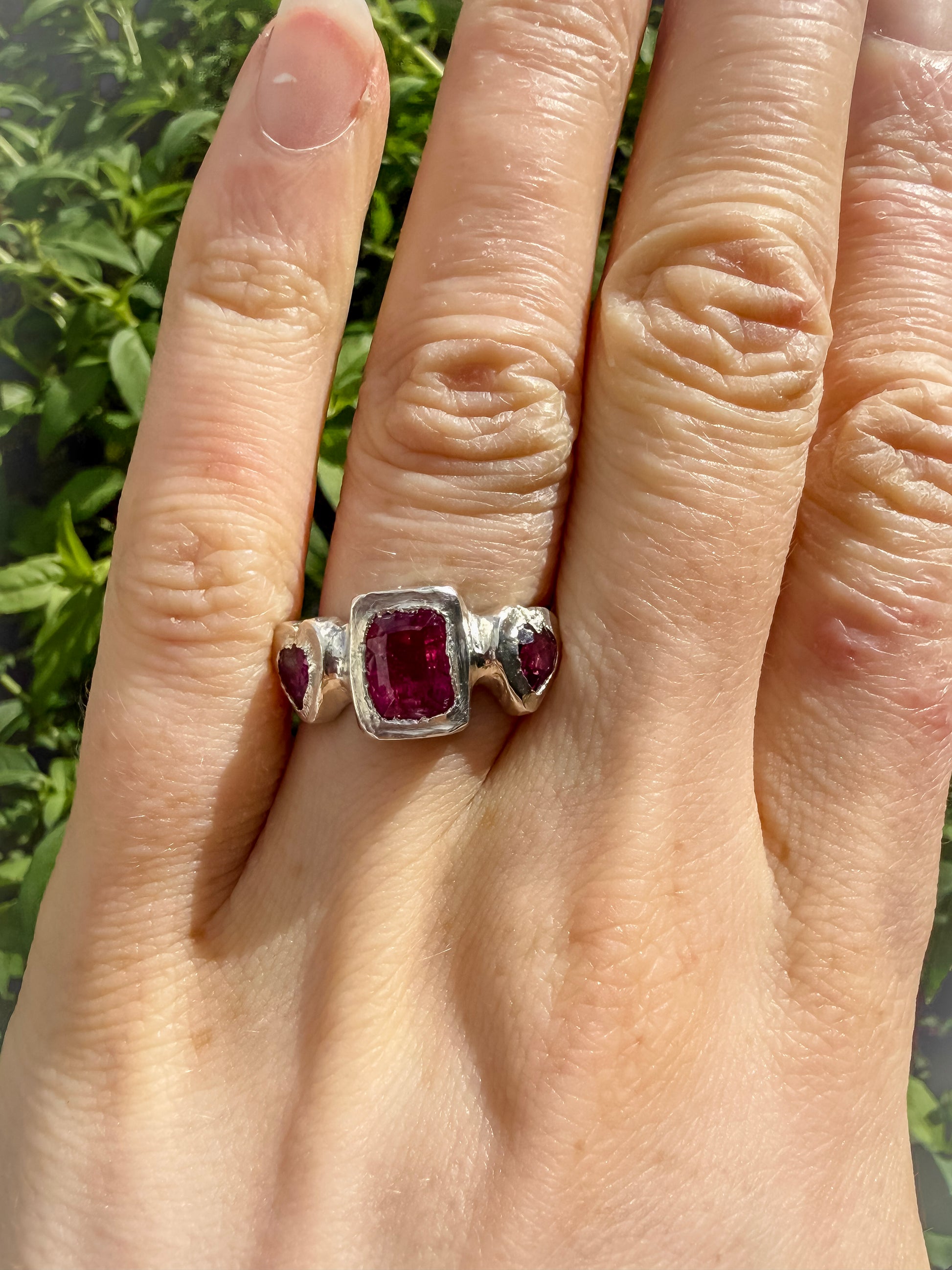 Octagon_cushion_cut_hot_pink_tourmaline_and_purple_rhodolite_heart_handmade_silver_ring_on_hand_against_leafy_background
