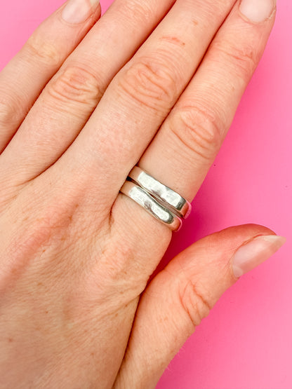 Hand wearing a silver ring on a pink background