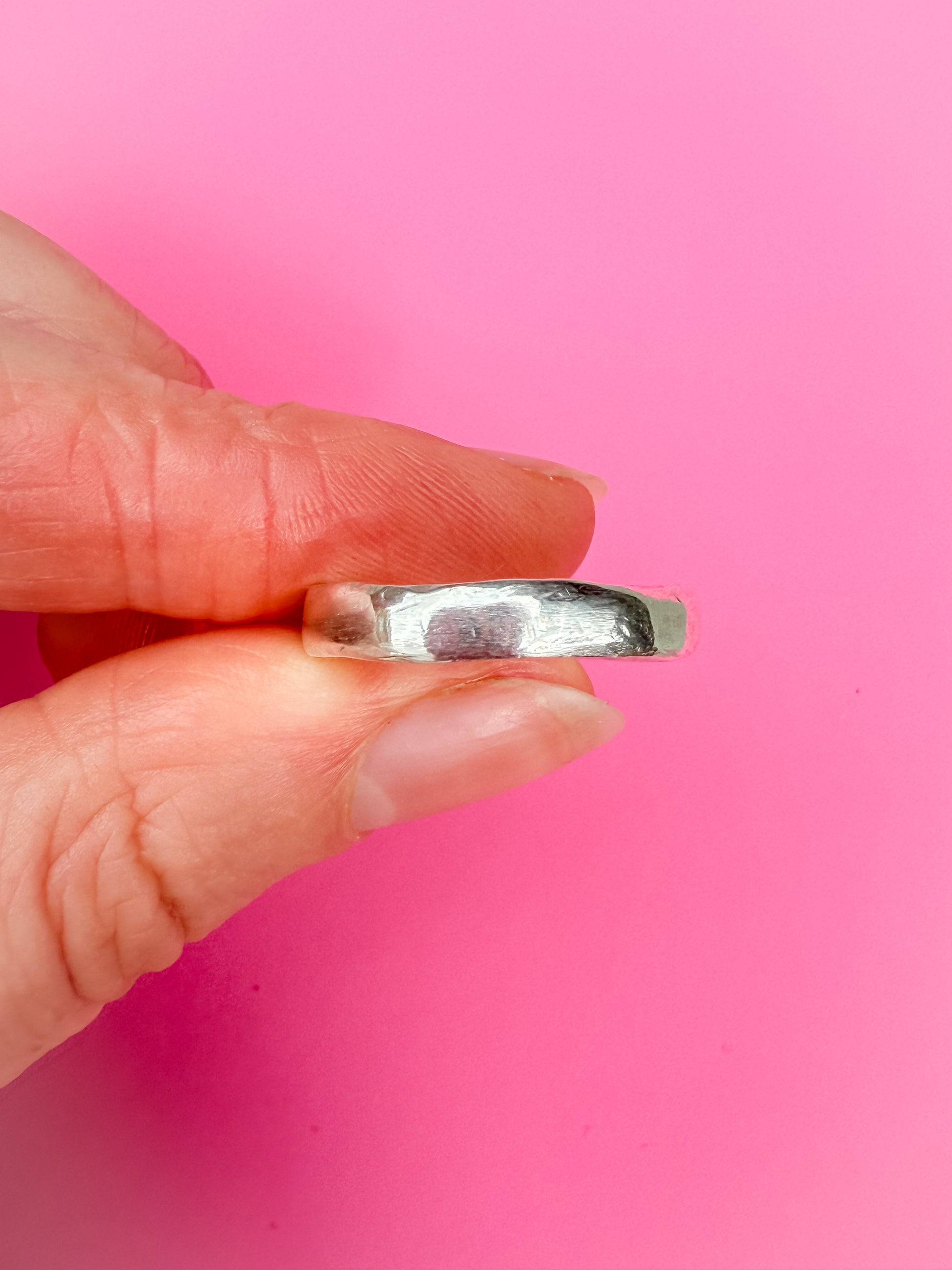 Hand holding a silver ring against a pink background