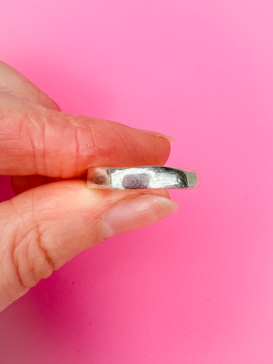 Hand holding a silver ring against a pink background