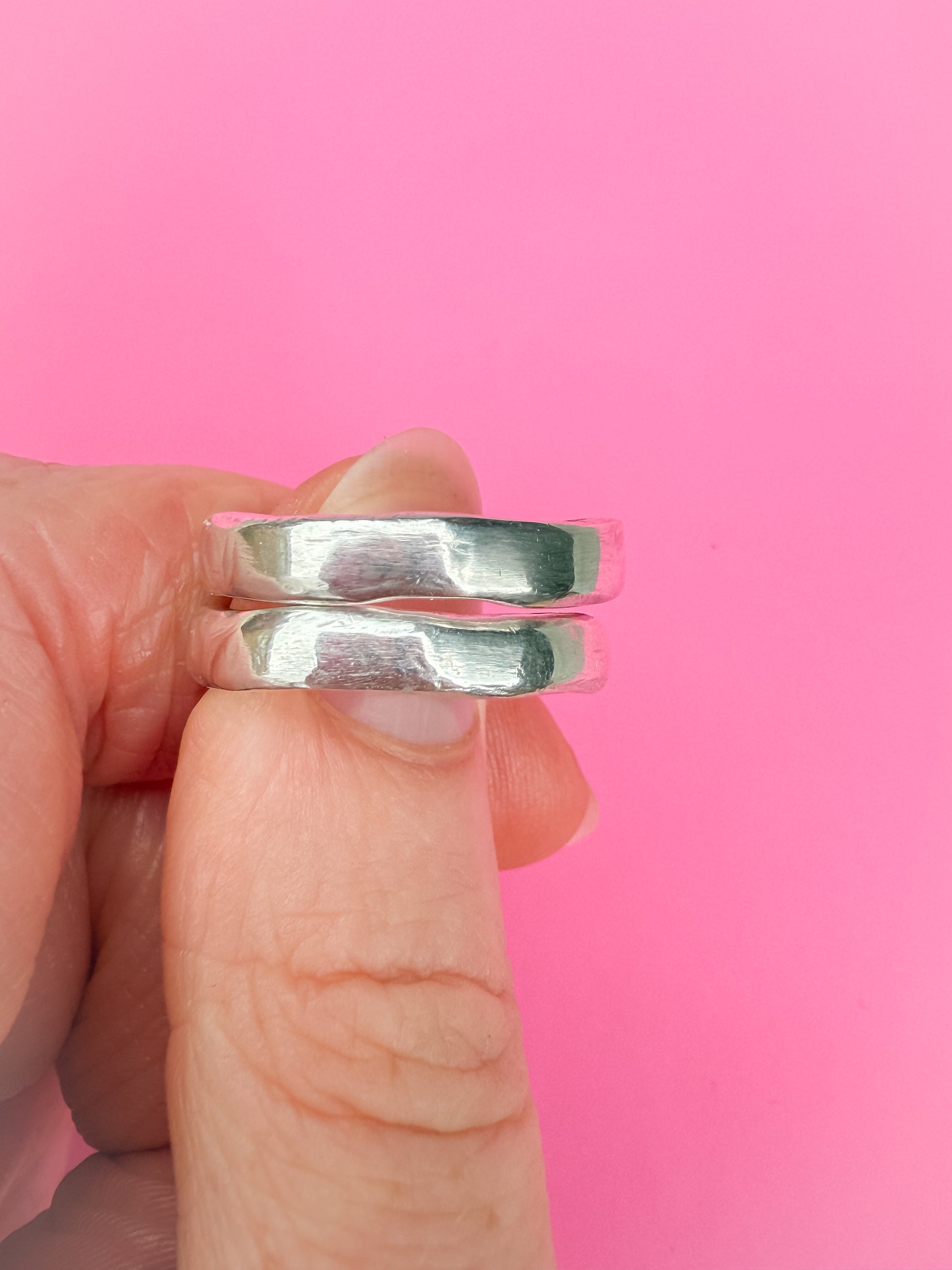 Silver rings held between fingers against a pink background