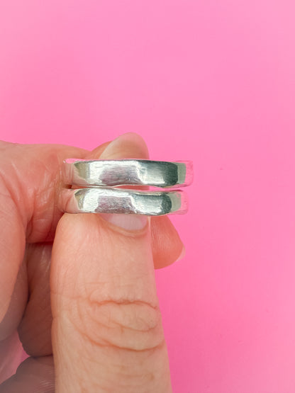 Silver rings held between fingers against a pink background
