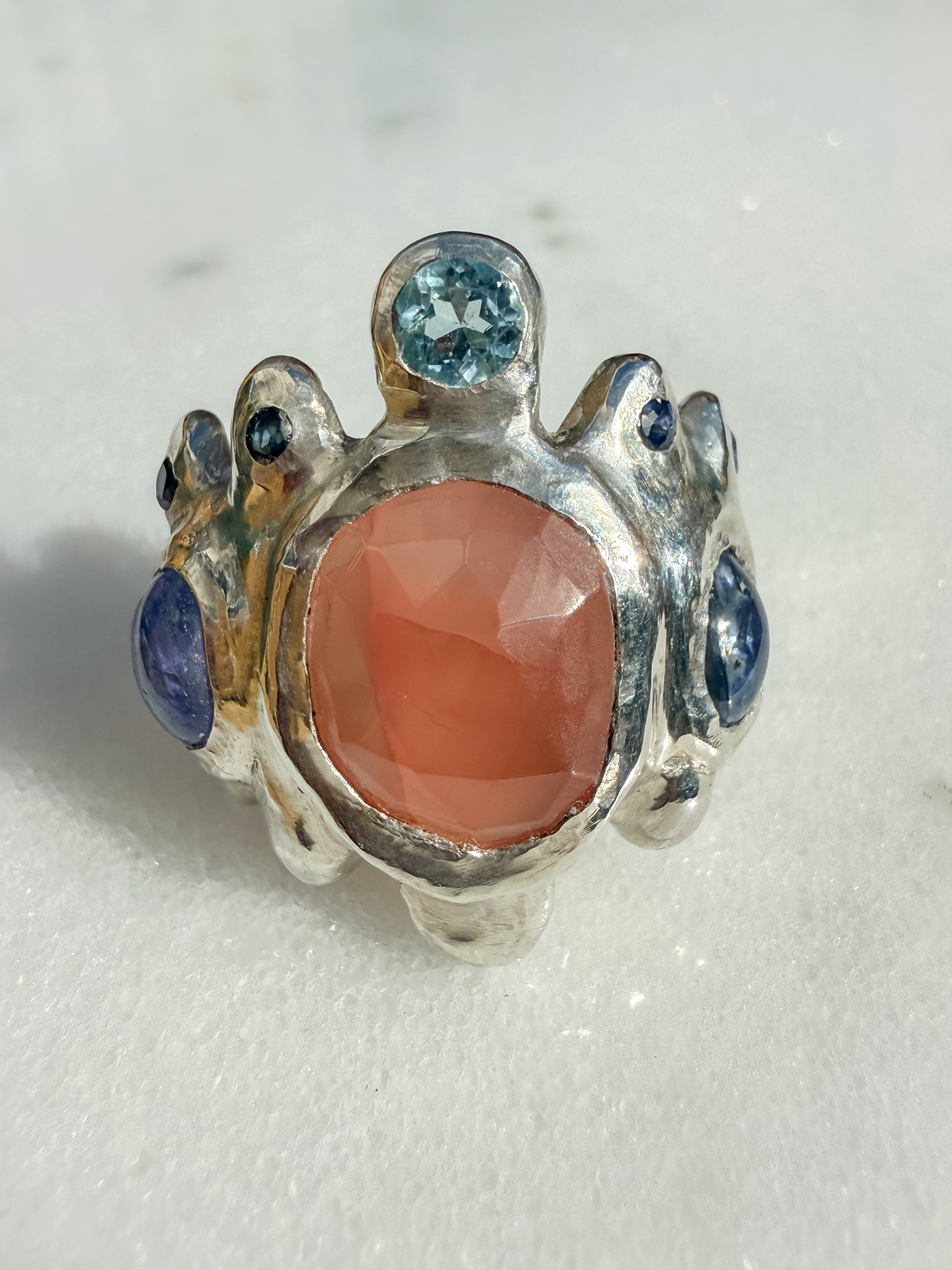 Silver ring with a pink stone and blue gemstones on a white background