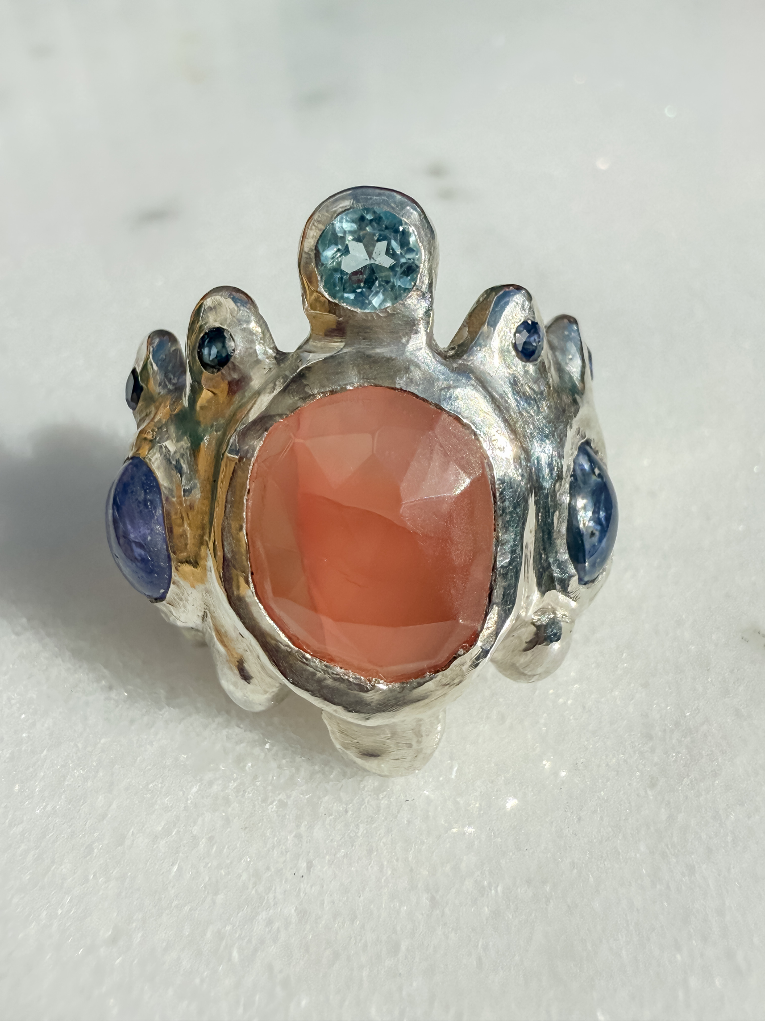 Silver ring with a pink stone and blue gemstones on a white background