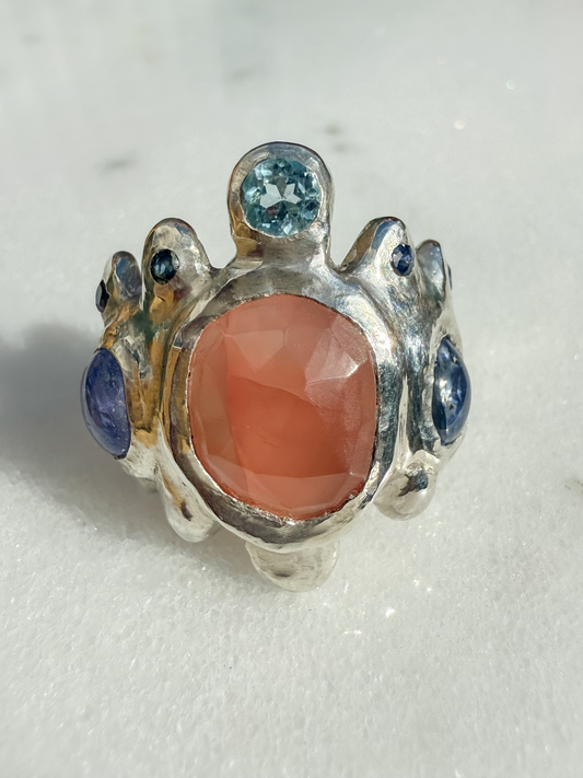 Silver ring with a pink stone and blue gemstones on a white background