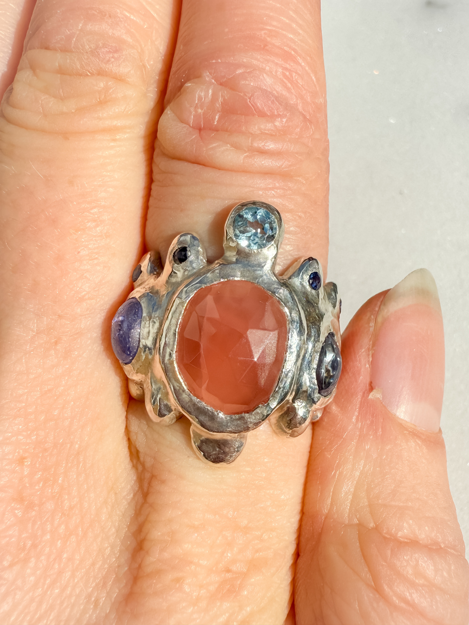 Silver ring with a large orange stone and smaller purple stones on a finger.