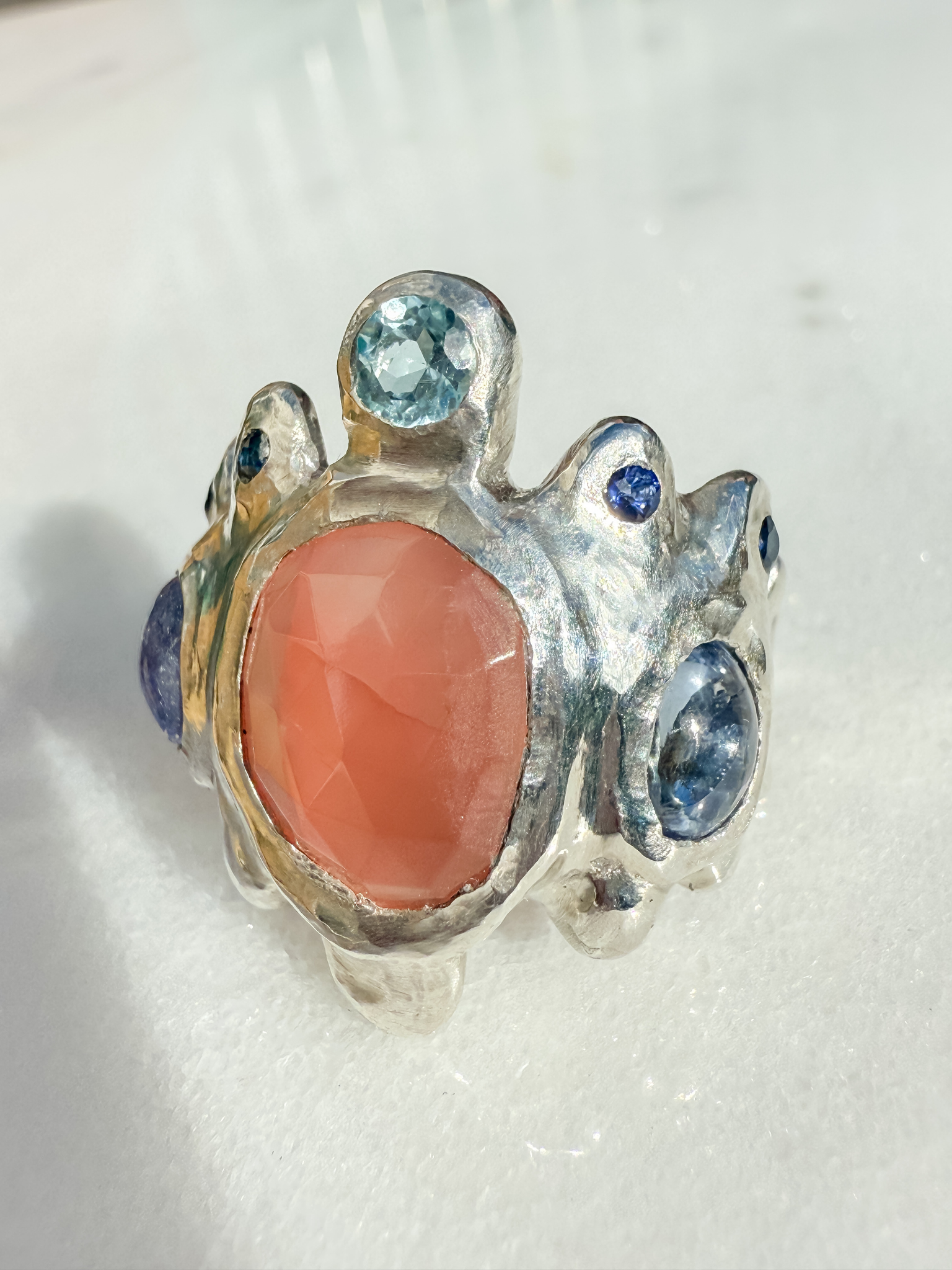 Silver ring with a pink stone and blue gemstones on a white background