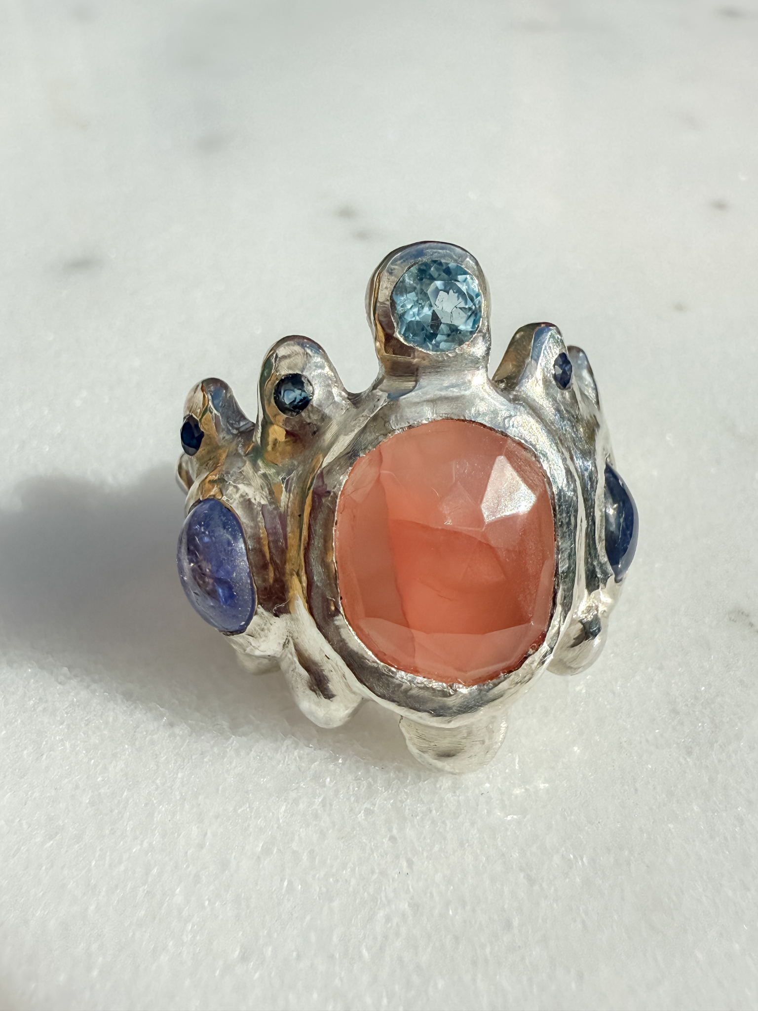 Silver ring with a pink stone and blue gemstones on a light background