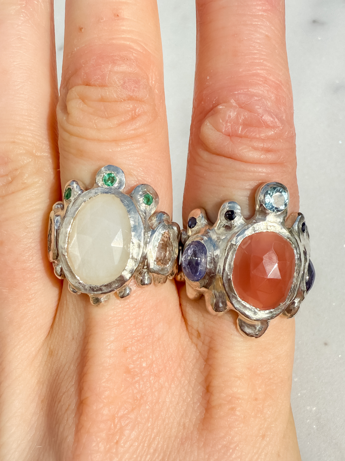 Two silver rings with gemstones on a hand against a neutral background