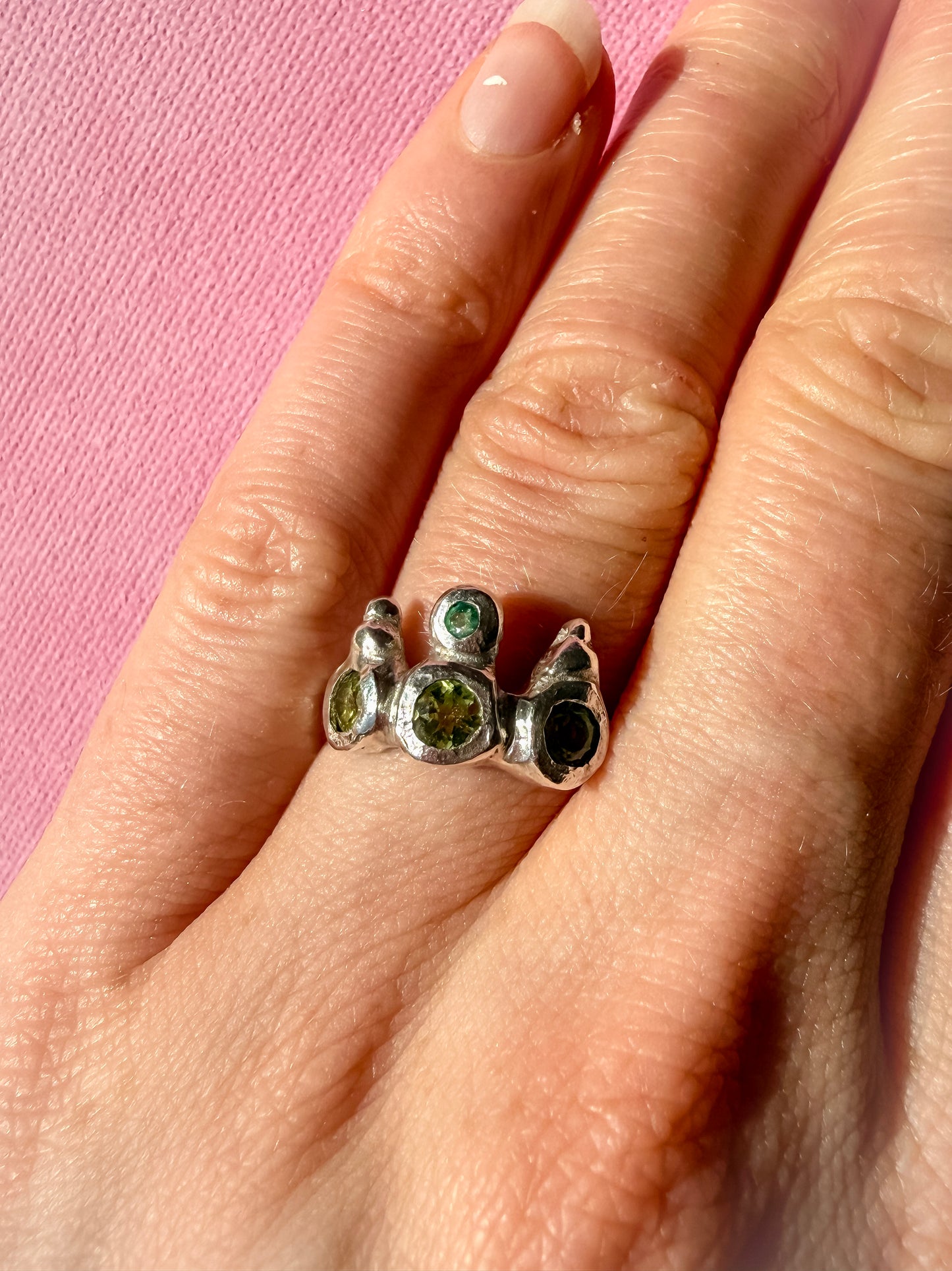 Peridot and emerald handmade silver ring on hand against pink background