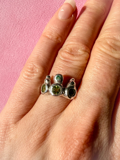 Peridot and emerald handmade silver ring on hand against pink background