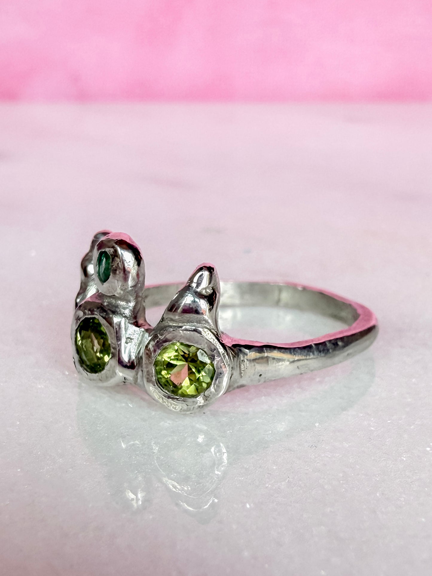 Peridot and emerald handmade silver ring other side view on marble surface