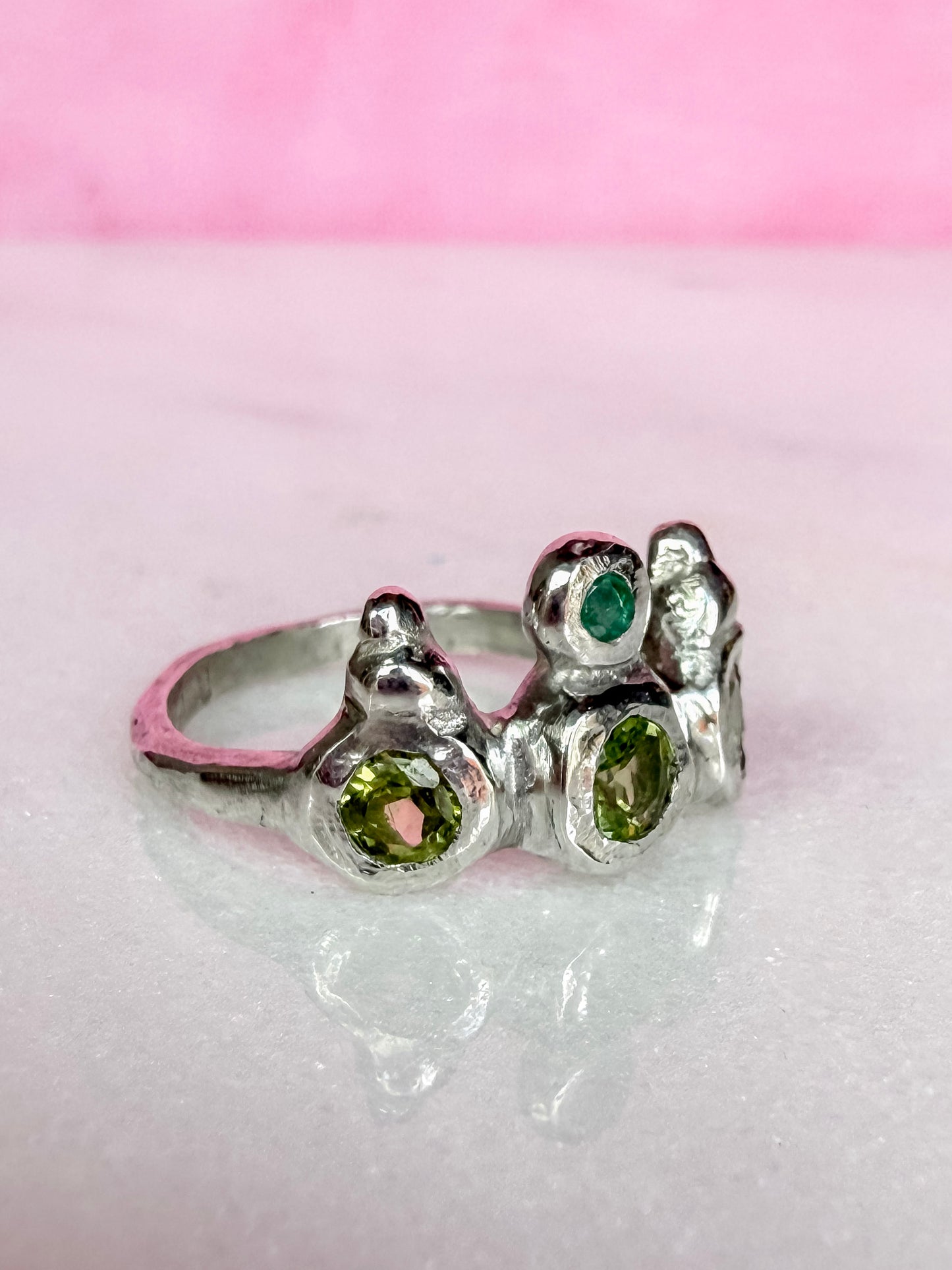Peridot and emerald handmade silver ring side view on marble surface
