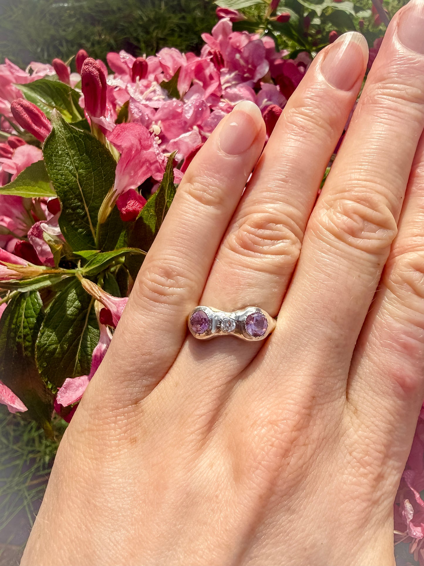 Hand wearing a ring with pink gemstones against a floral background