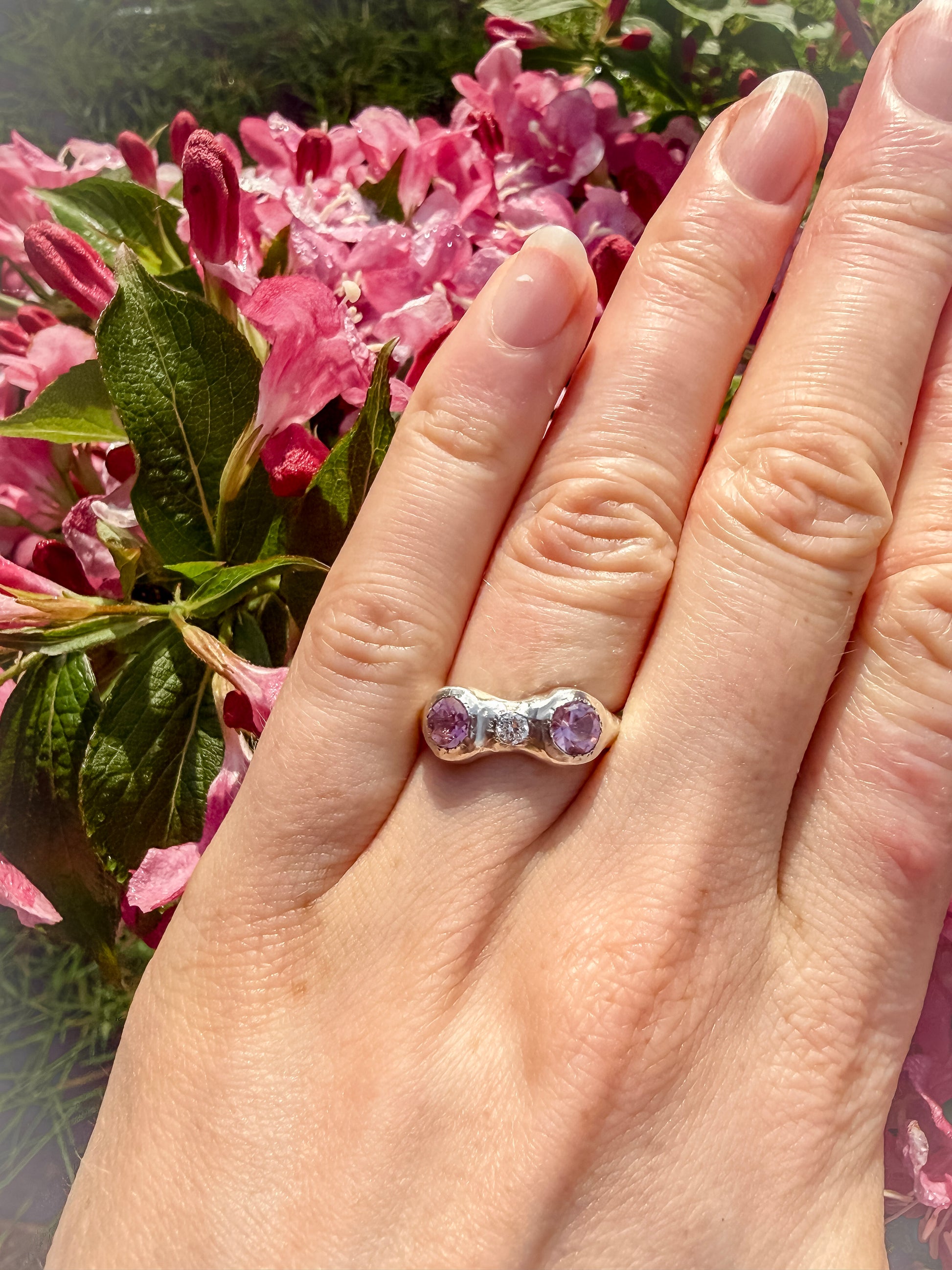 Hand wearing a ring with pink gemstones against a floral background