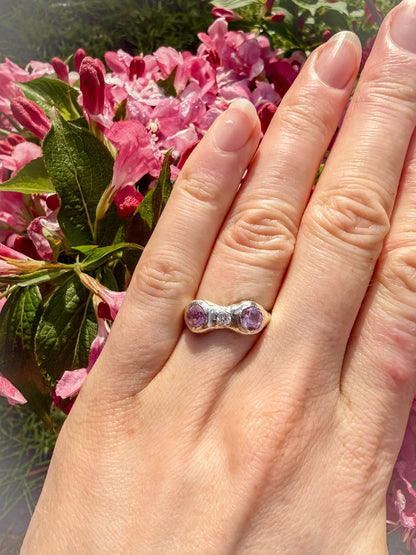 Hand wearing a ring with pink gemstones against a floral background