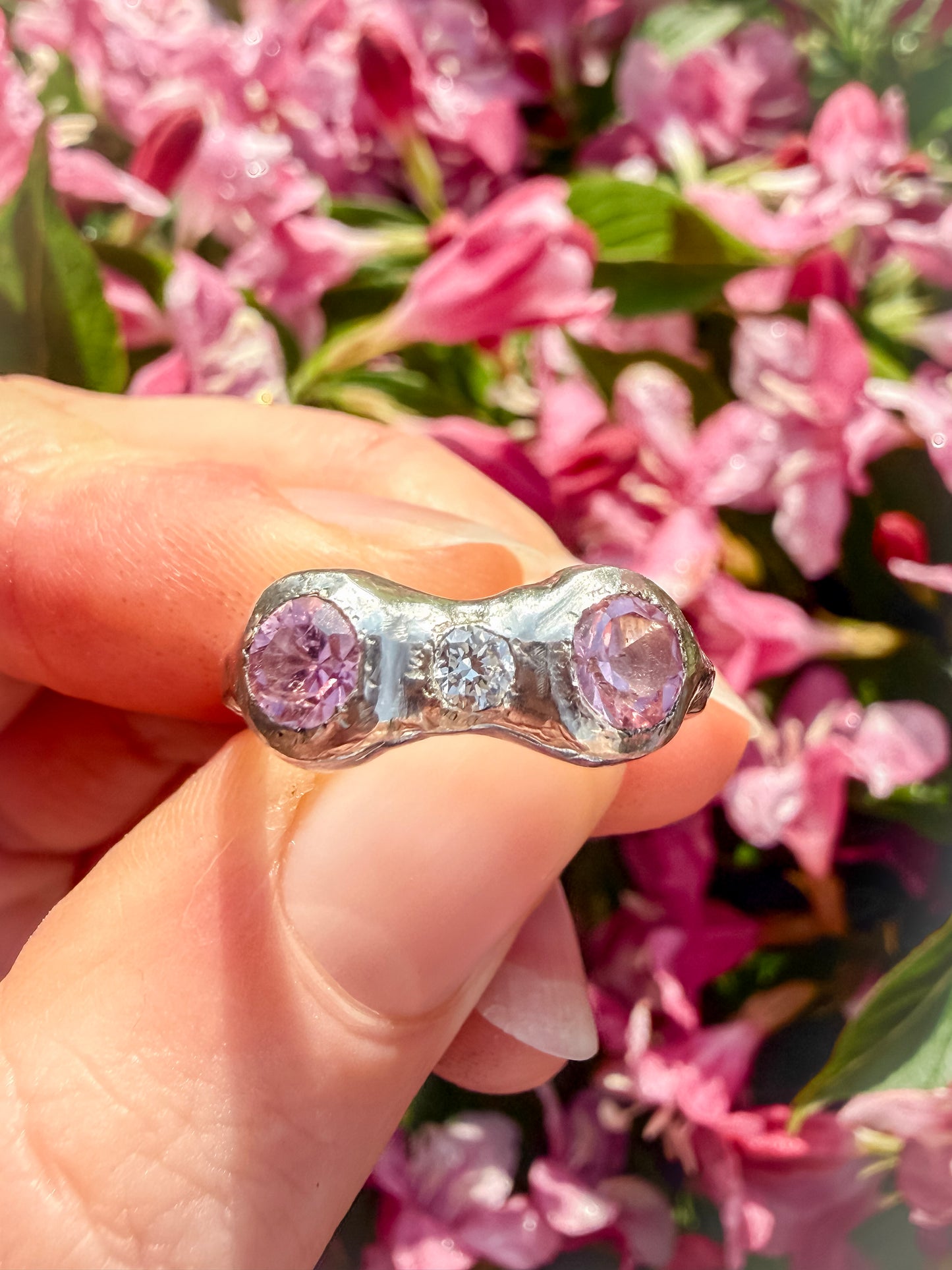 Ring with pink gemstones held in front of pink flowers