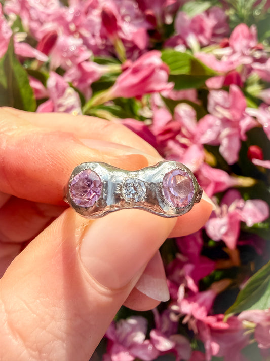 Ring with pink gemstones held in front of pink flowers