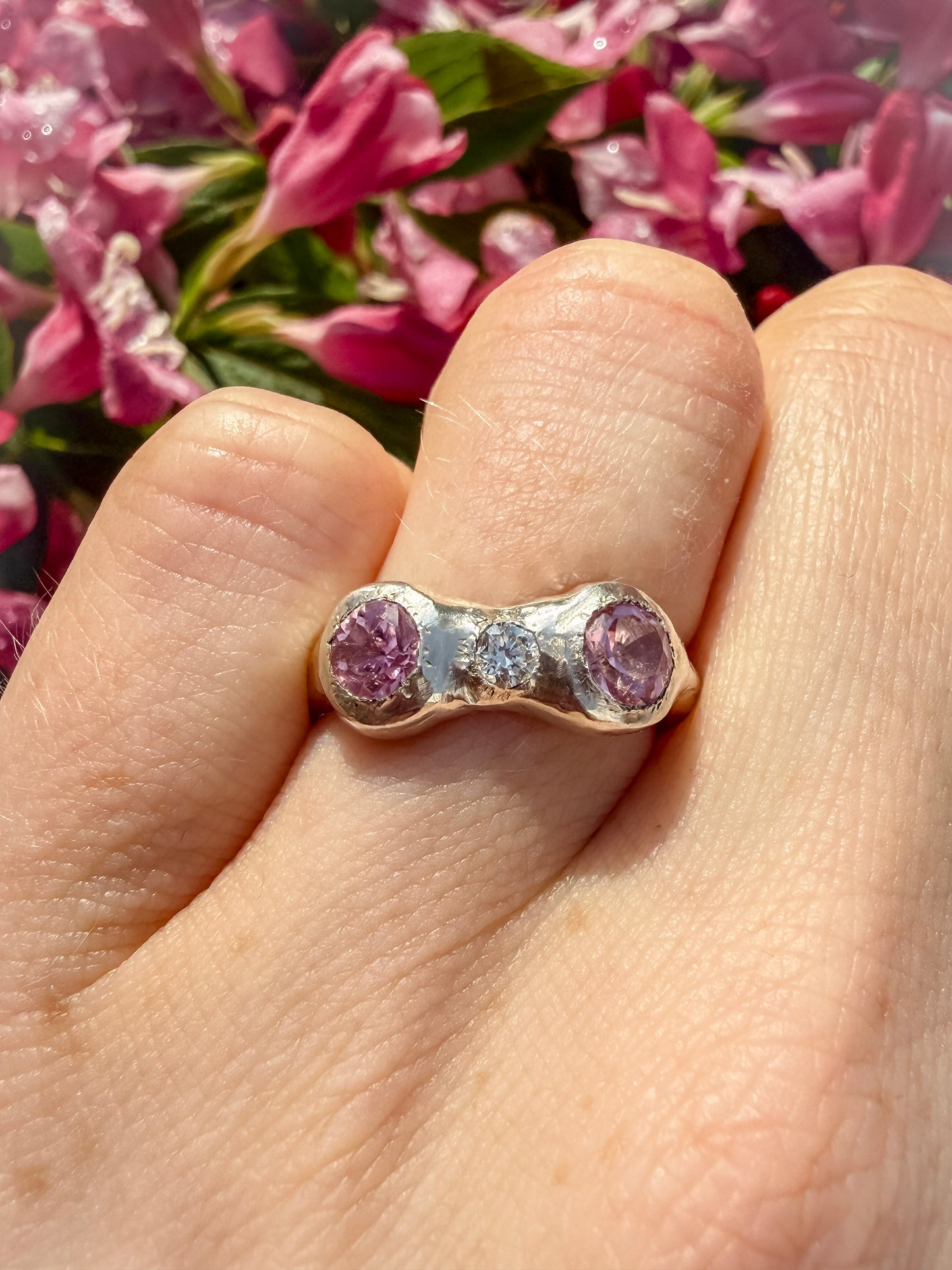 Ring with pink gemstones on a finger against a floral background