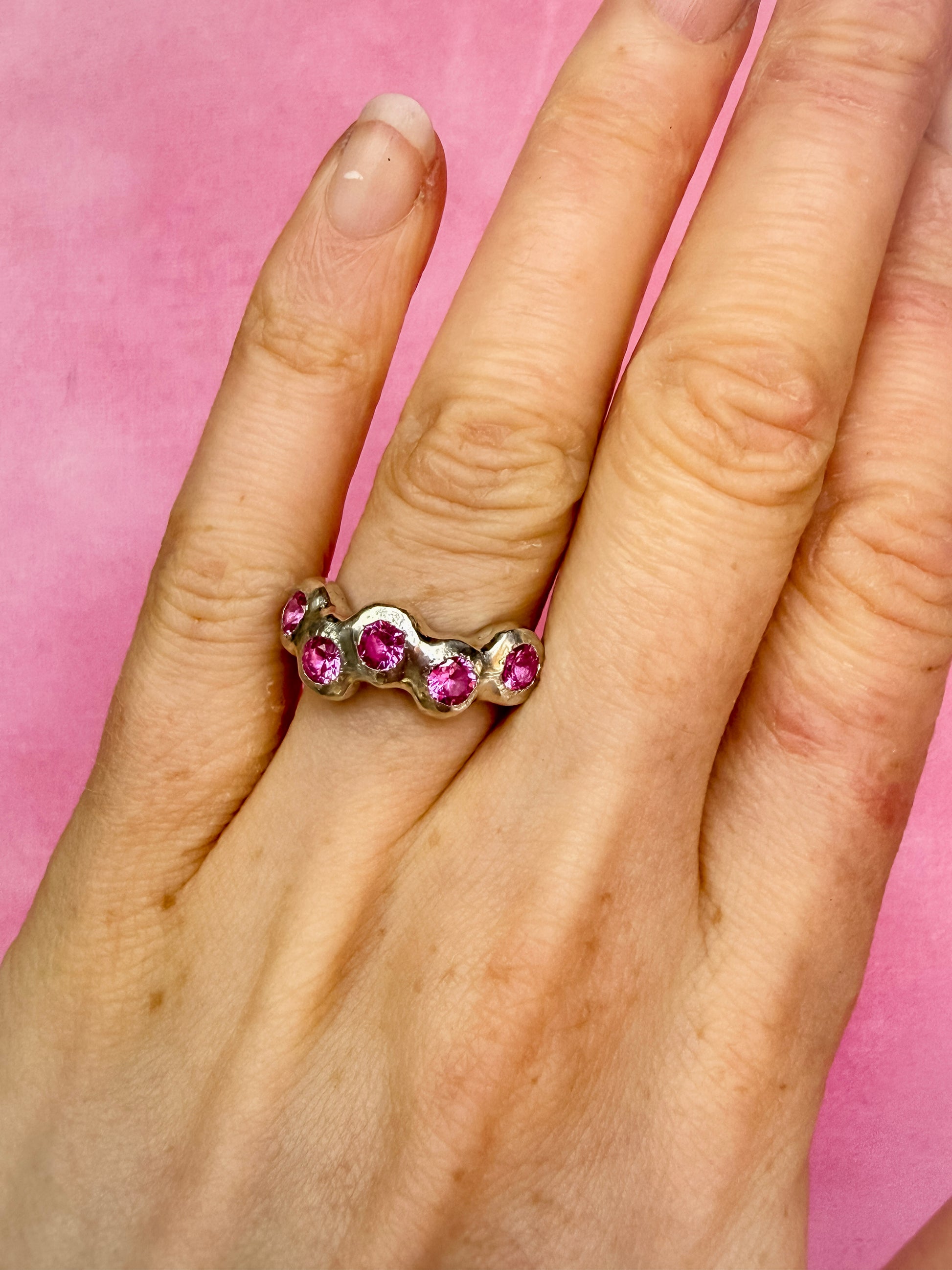 Pink Lab-Grown Sapphire Silver Handmade Ring on hand against pink background