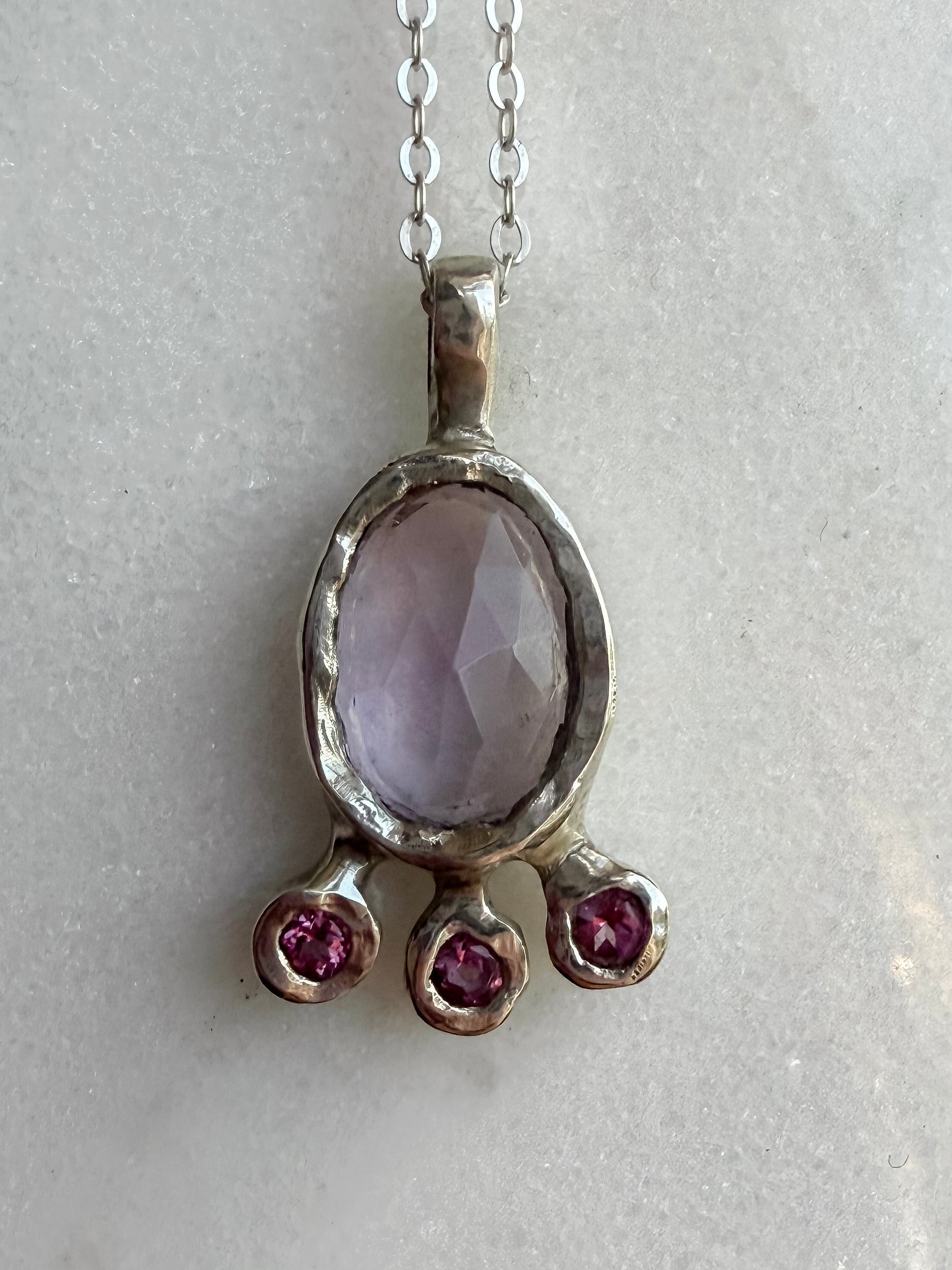 Pink amethyst slice and pink topaz silver pendant on marble surface