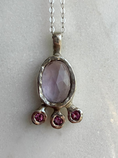 Pink amethyst slice and pink topaz silver pendant on marble surface