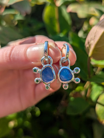 Silver Australian opal earrings with blue stones held in a hand against a green leafy background