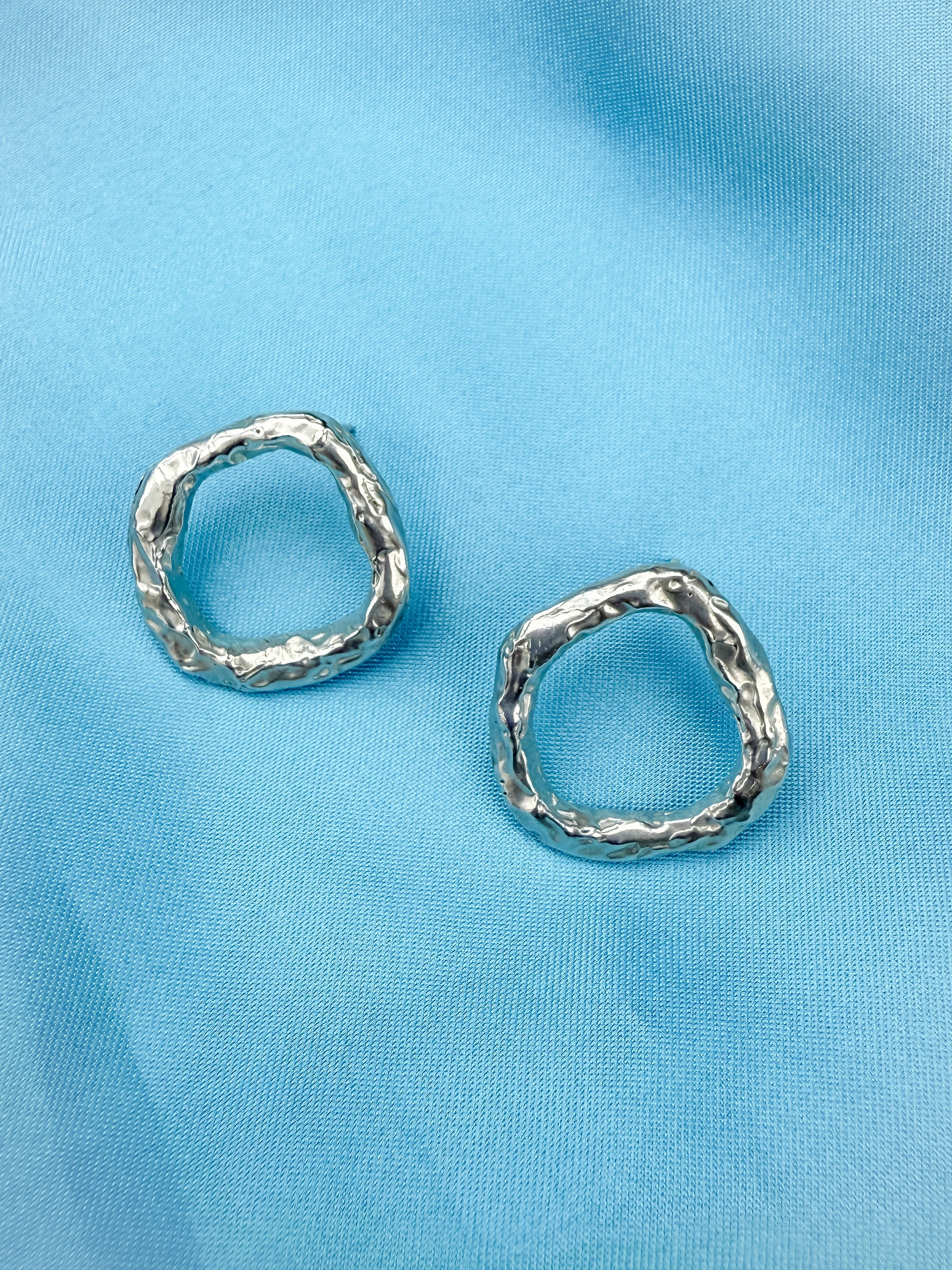 Pair of silver circle stud earrings on blue background
